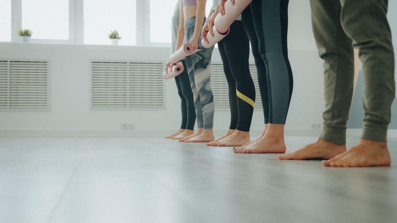 A group of people in leggings ready for a yoga class in a bright studio.