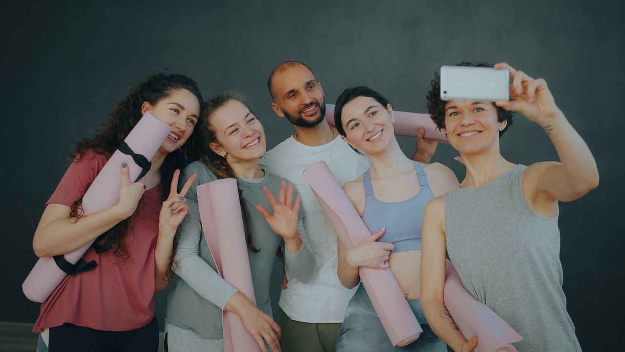 Diverse group of friends taking a selfie post-yoga, smiling with mats in hand.