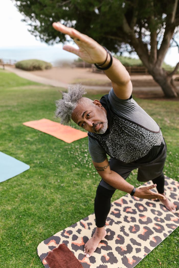 A senior man in activewear practicing yoga in a sunny park setting, promoting wellness and fitness.